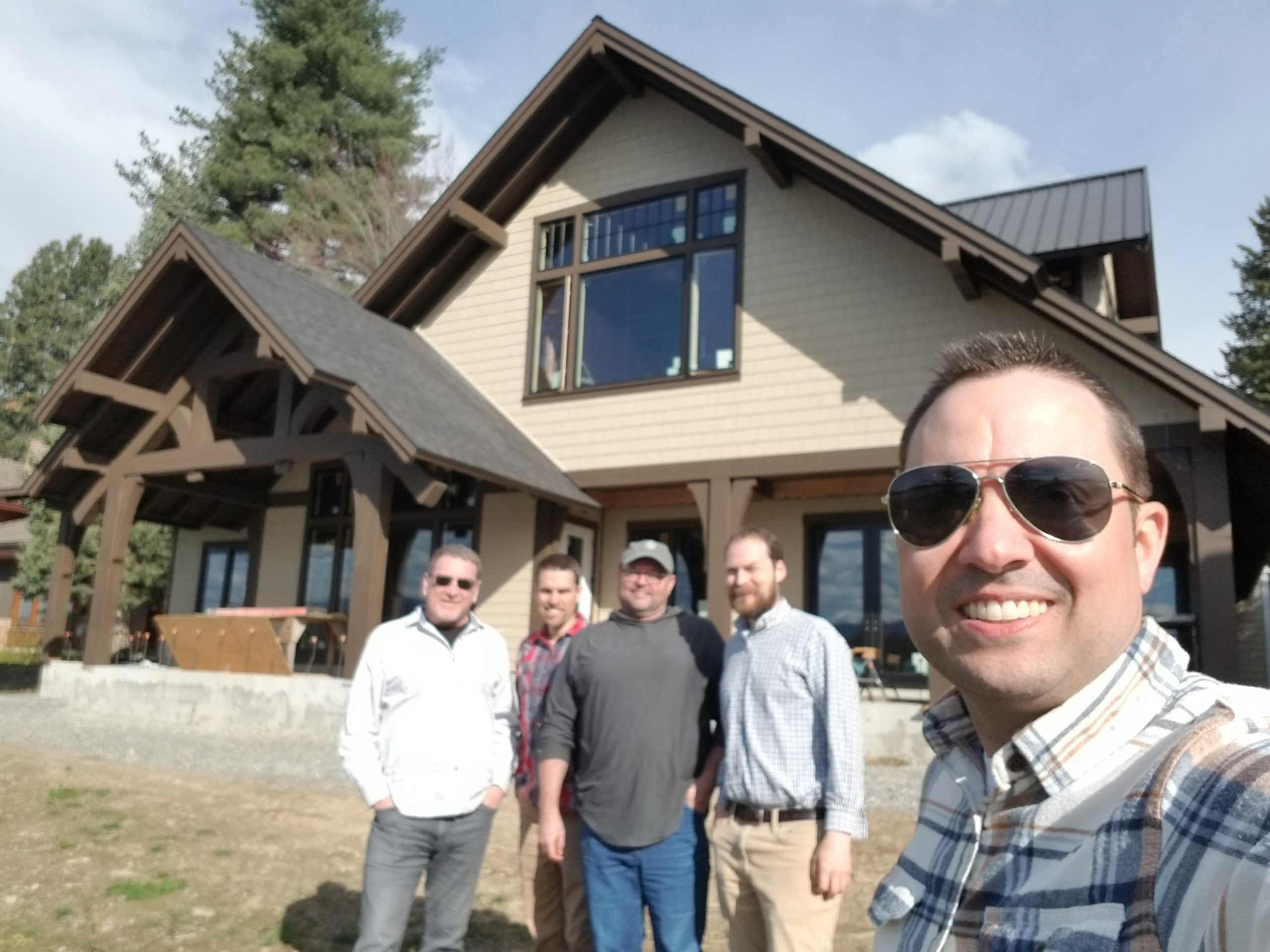 this is a raking selfie of 5 mountain home architects who are happy and standing in front of a nearly completed mountain craftsman home.